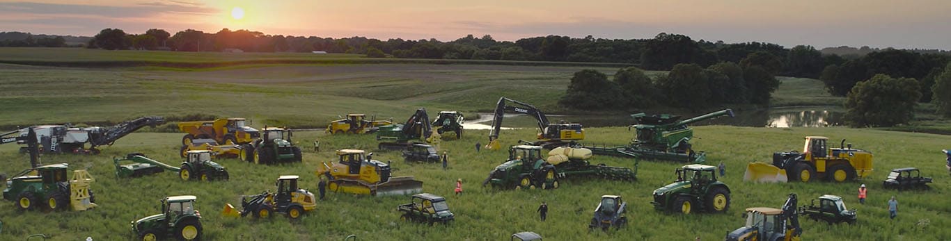 Personnes se déplaçant parmi plusieurs types d’équipements John Deere dans un grand champ.