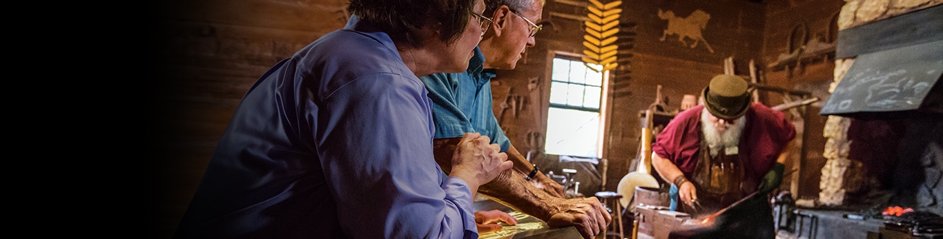 Ouder echtpaar kijkt naar de smid met een stuk van een metalen hamer op de historische locatie in Grand Detour, Illinois, Verenigde Staten