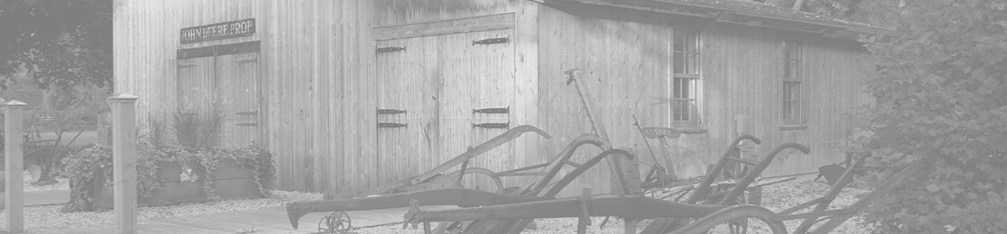 Photographie en noir et blanc teintée de la reconstitution du site historique de l’atelier de forgeron d’origine de John Deere sur fond vert