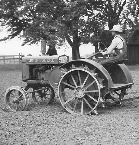 Historische GP-tractor (General Purpose, algemeen gebruik) van John Deere trekt een John Deere nr. 7 bodemfrees in het veld