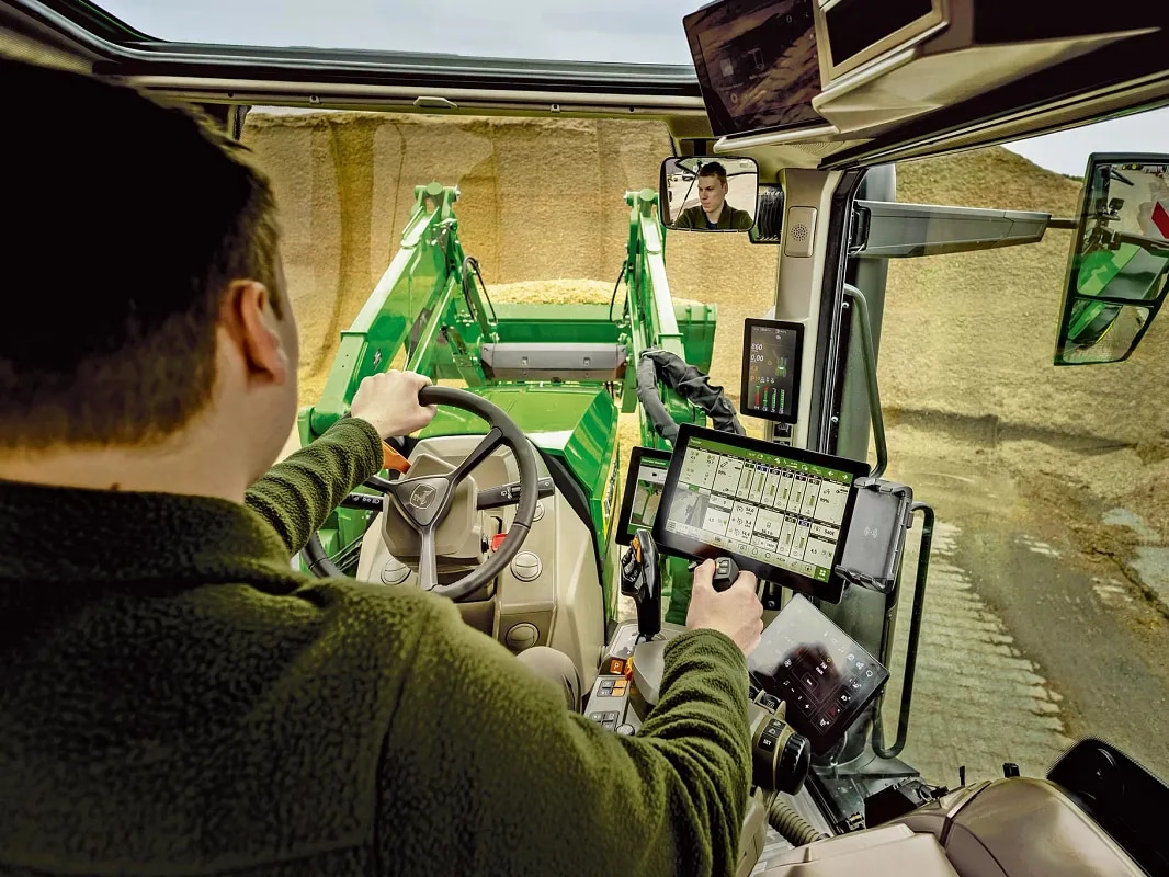 Vue de l’intérieur de la cabine d’un tracteur John&nbsp;Deere montrant les commandes de l’utilisateur et le fonctionnement du chargeur frontal.