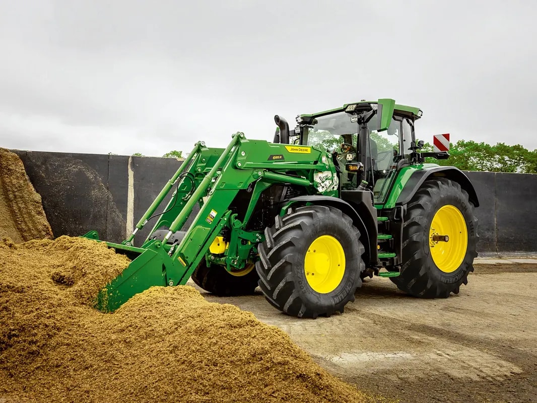 Tracteur John&nbsp;Deere en train de pousser un tas d’ensilage à l’aide du godet de son chargeur frontal, dans un environnement agricole.