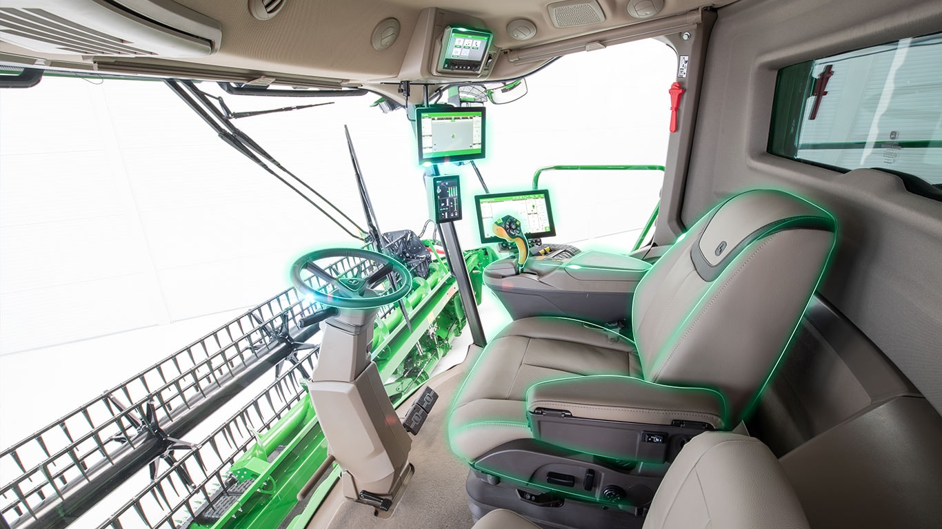 Intérieur de cabine de moissonneuse-batteuse avec ses consoles d’agriculture de précision, son volant et son unité de récolte visible à travers le pare-brise avant