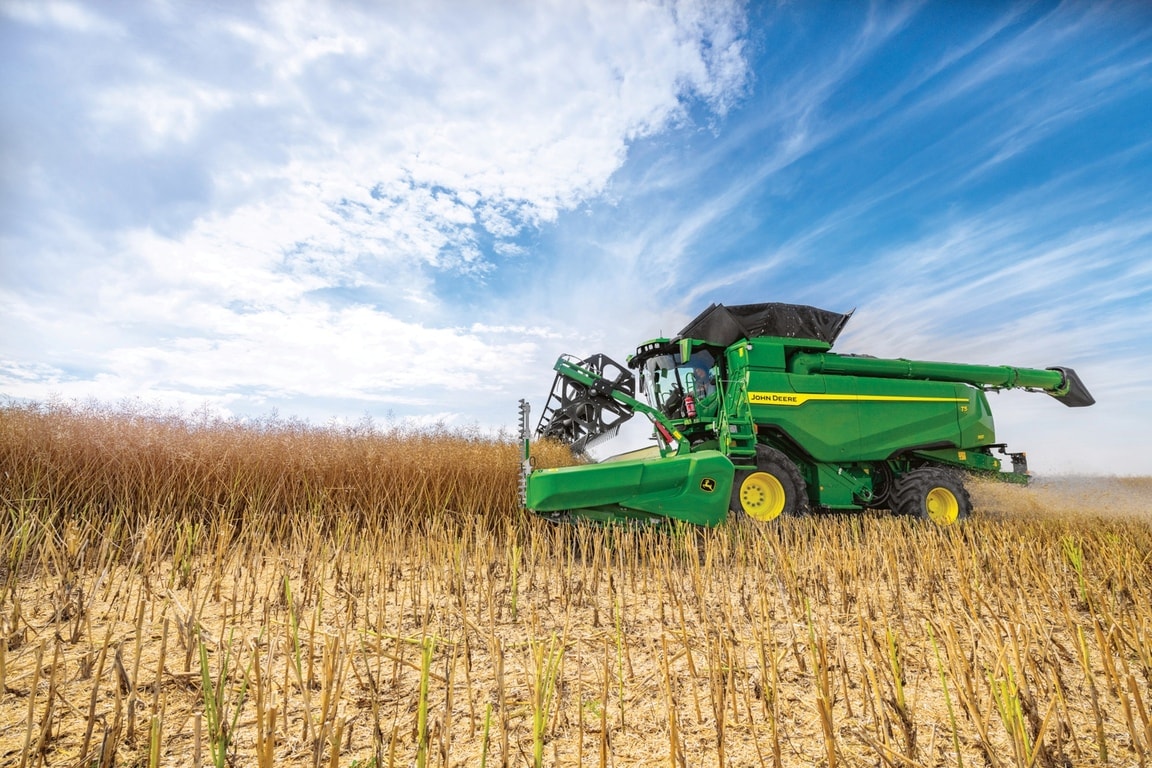 Une moissonneuse-batteuse John Deere récolte des céréales avec son unité de récolte dans un champ sous un ciel bleu