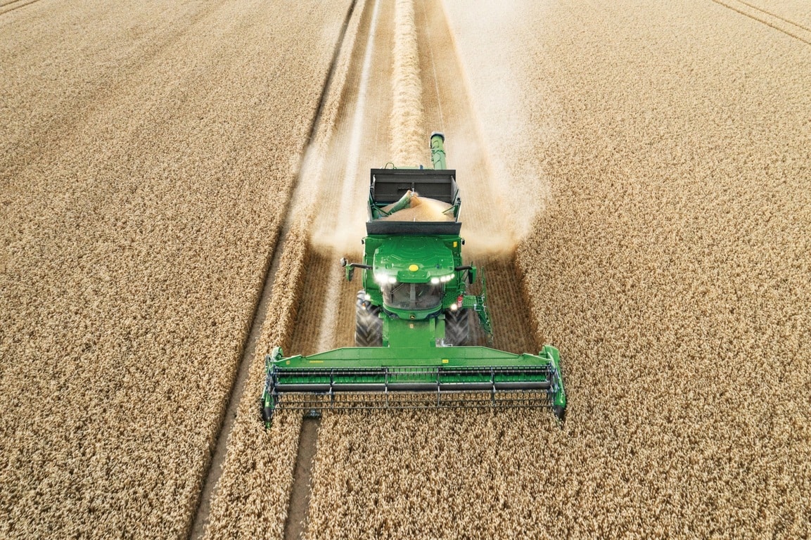 Moissonneuse-batteuse déchargeant le grain tout en moissonnant un champ de blé, avec une unité de récolte fonctionnant efficacement