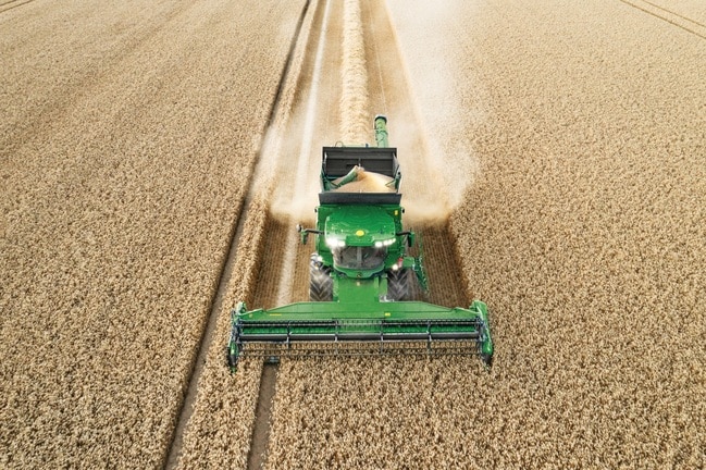 Moissonneuse-batteuse déchargeant le grain tout en moissonnant un champ de blé, avec une unité de récolte fonctionnant efficacement