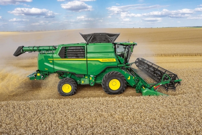 Vue de profil d’une moissonneuse-batteuse John Deere équipée d’une unité de récolte, en train de récolter du blé dans un vaste champ