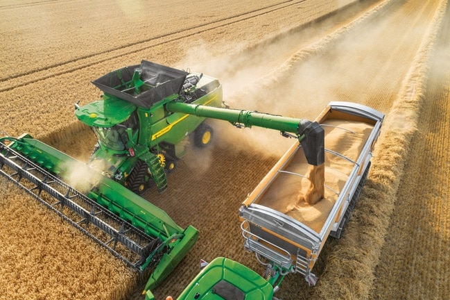Combineer het lossen van graan in de aanhangwagen tijdens de tarweoogst met stofwolken die over het veld drijven