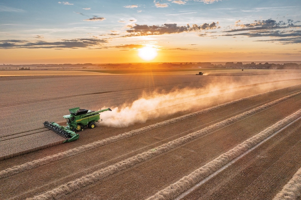 Combineer het oogsten van tarwe bij zonsondergang met een lang stofspoor dat zich uitstrekt over het uitgestrekte landbouwlandschap