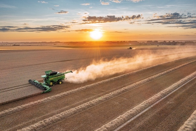 Combineer het oogsten van tarwe bij zonsondergang met een lang stofspoor dat zich uitstrekt over het uitgestrekte landbouwlandschap