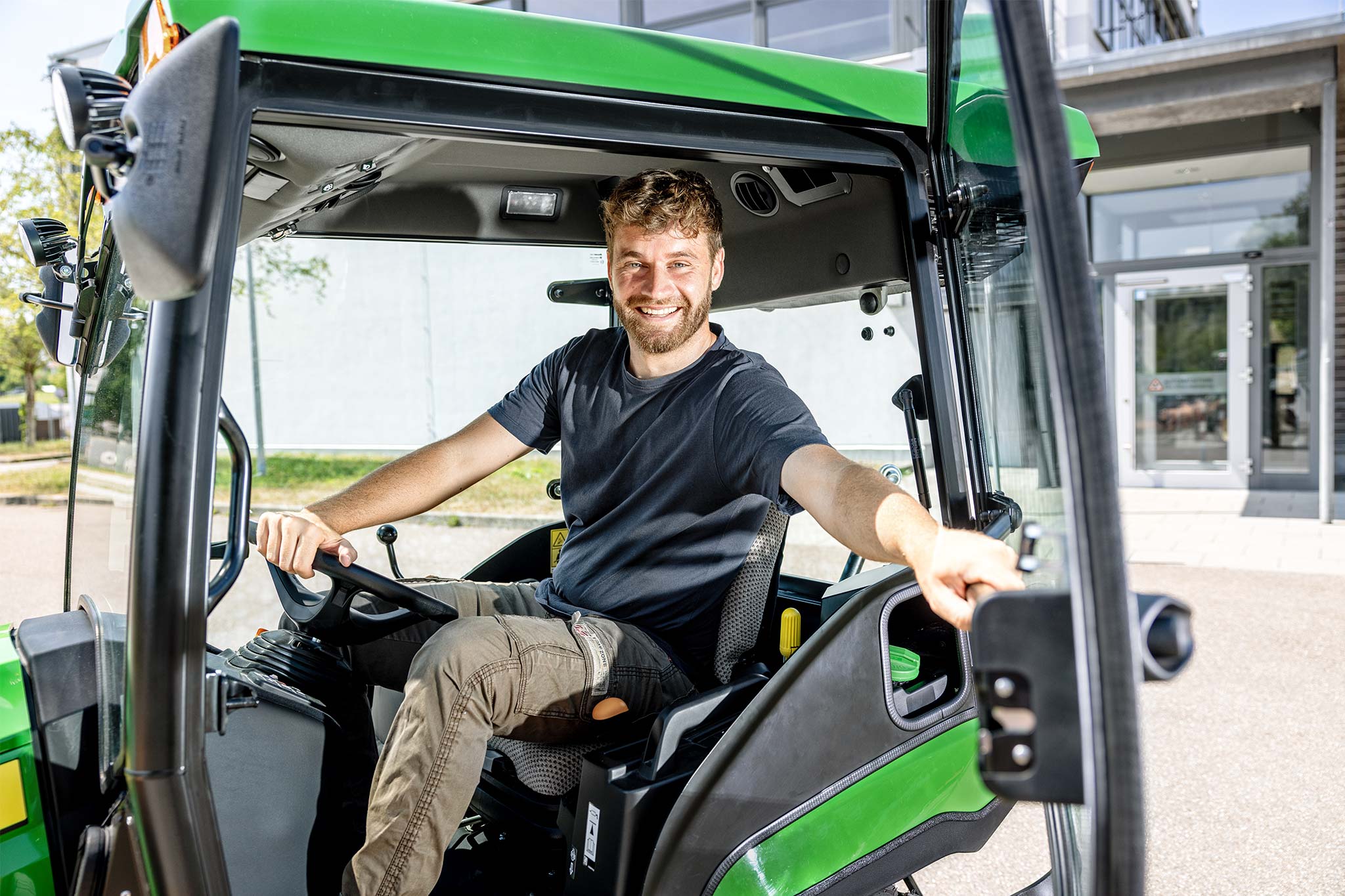 Un utilisateur assis dans la cabine d’un tracteur compact John Deere, la porte ouverte
