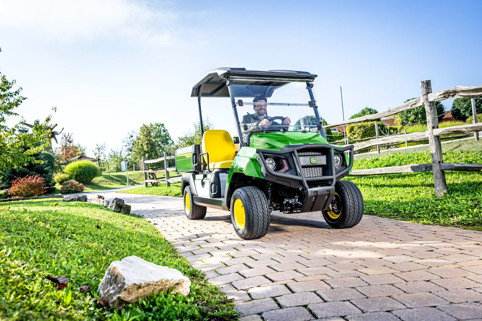 Véhicule utilitaire Gator GS roulant sur un chemin pavé dans un espace paysager Véhicule utilitaire Gator GS roulant sur un chemin pavé dans un espace paysager