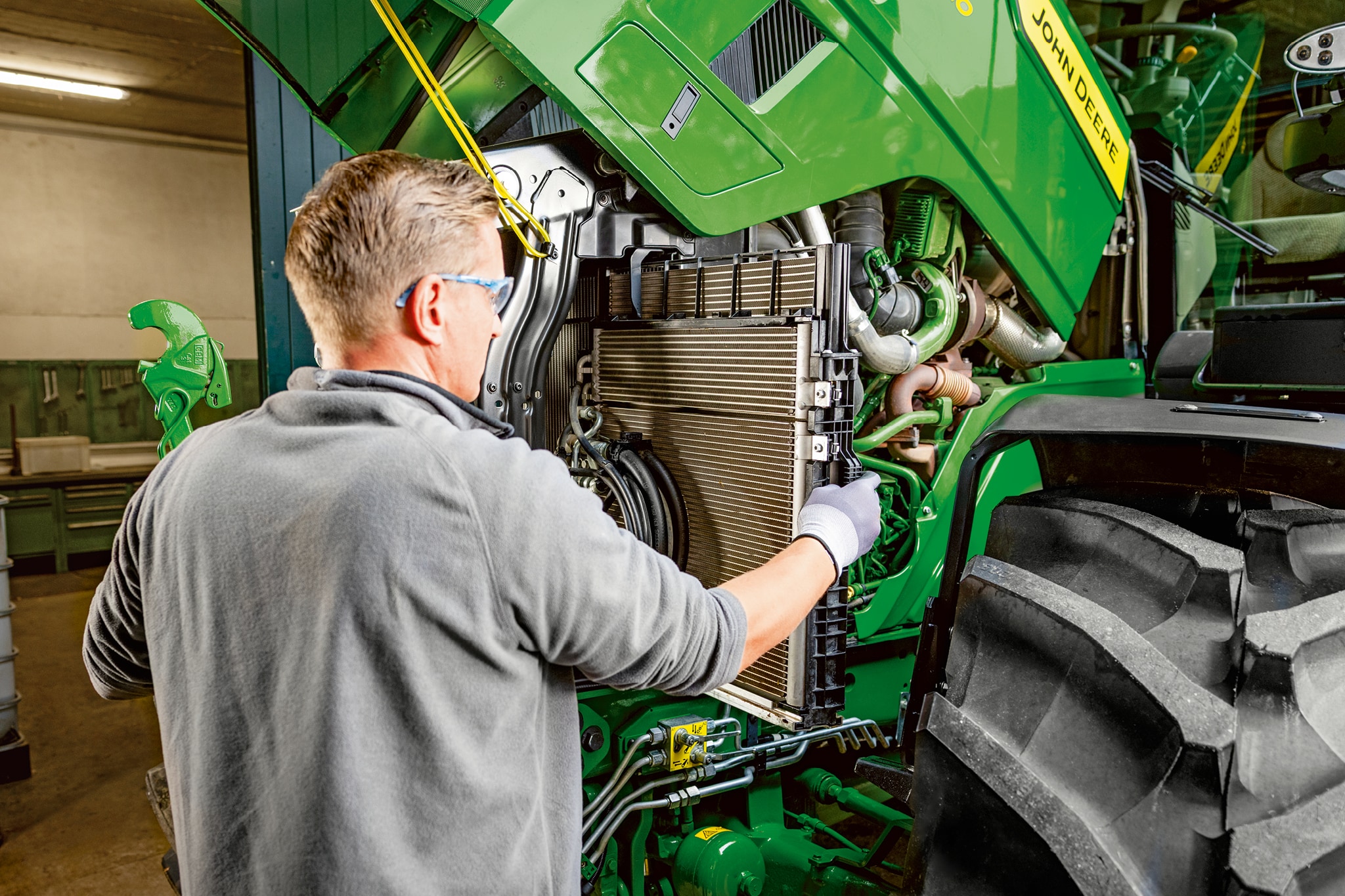 Servicemonteur die onderhoud uitvoert in het motorcompartiment van een John Deere 6M Series-tractor.