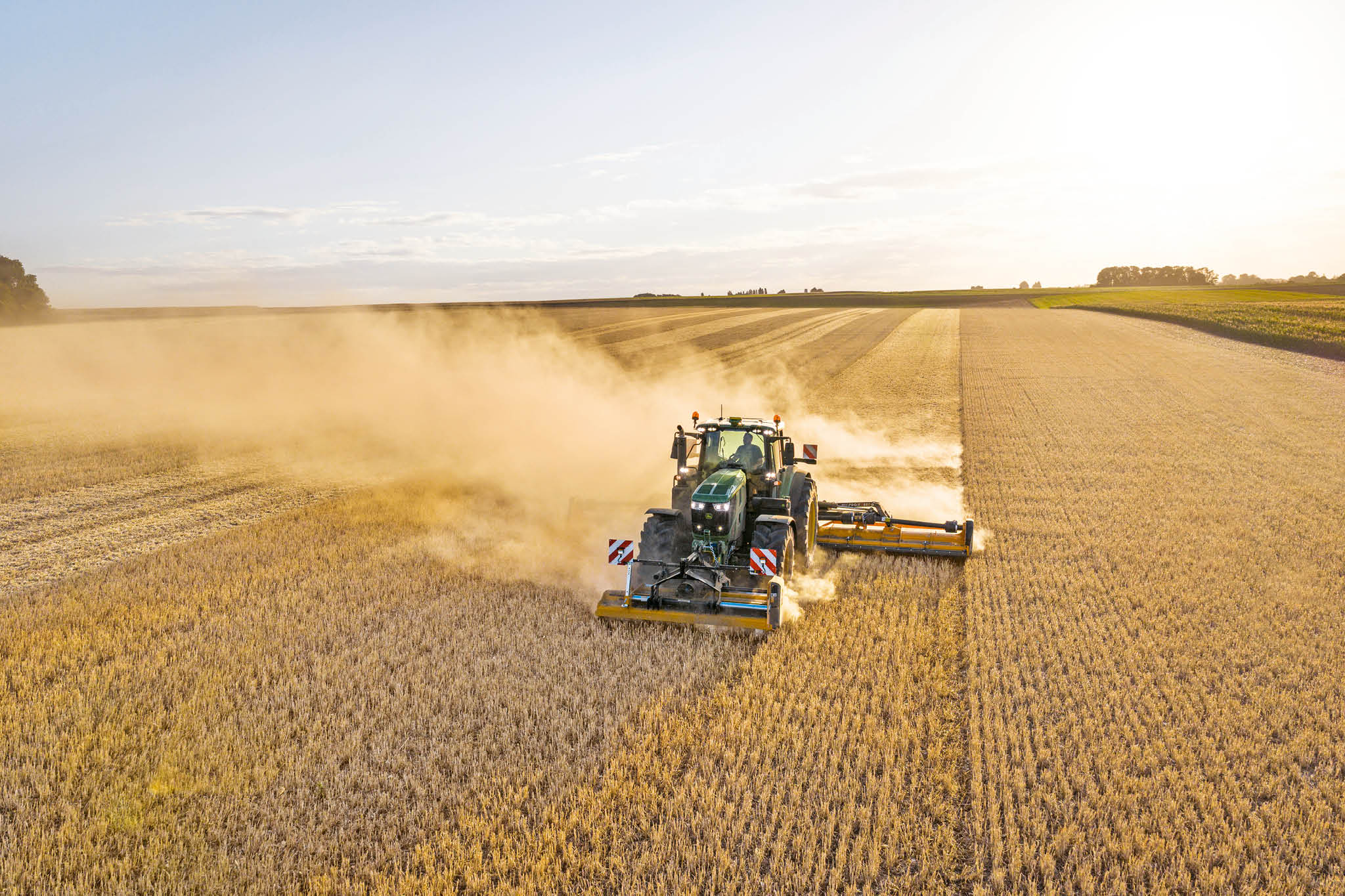 John Deere 6M Series-tractor die een mengmesttank trekt over een landelijke weg langs gras en velden.