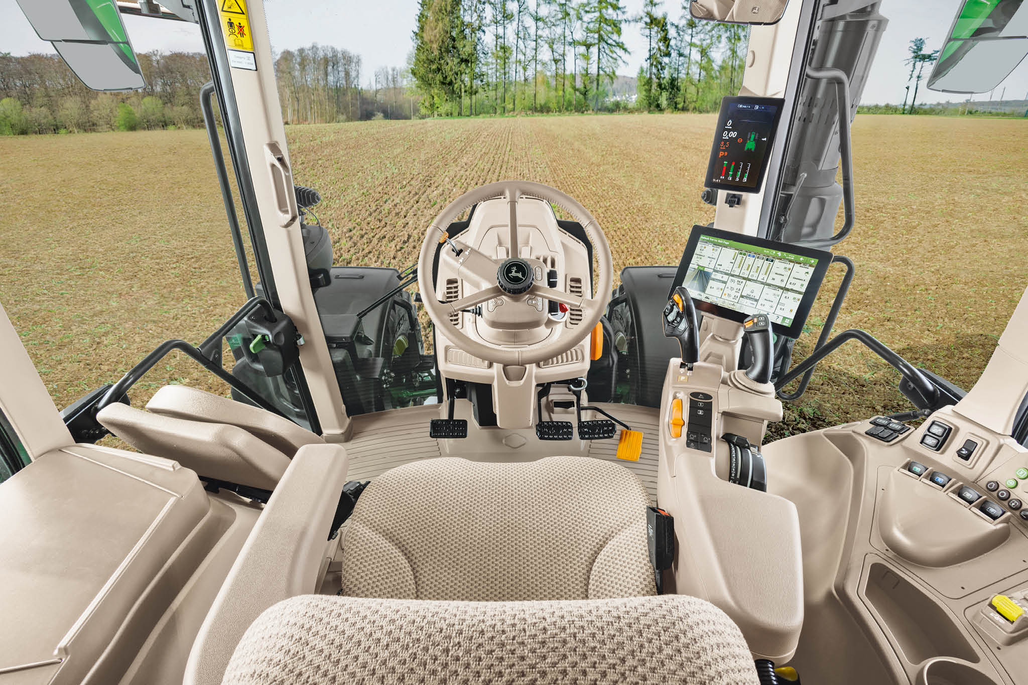 Binnenaanzicht van de cabine van een John Deere 6M Series-tractor met bestuurdersstoel, stuurwiel en digitale displays.