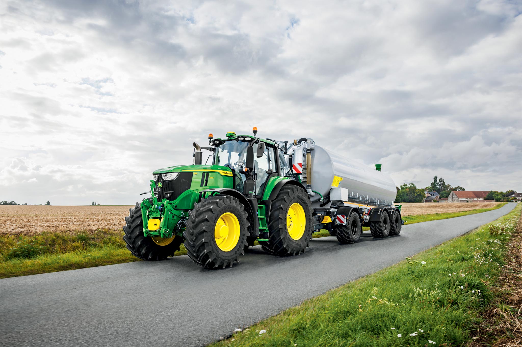 John Deere 6M Series-tractor die een geoogst veld bewerkt met brede cultivatoren, van bovenaf gezien met opwaaiend stof.