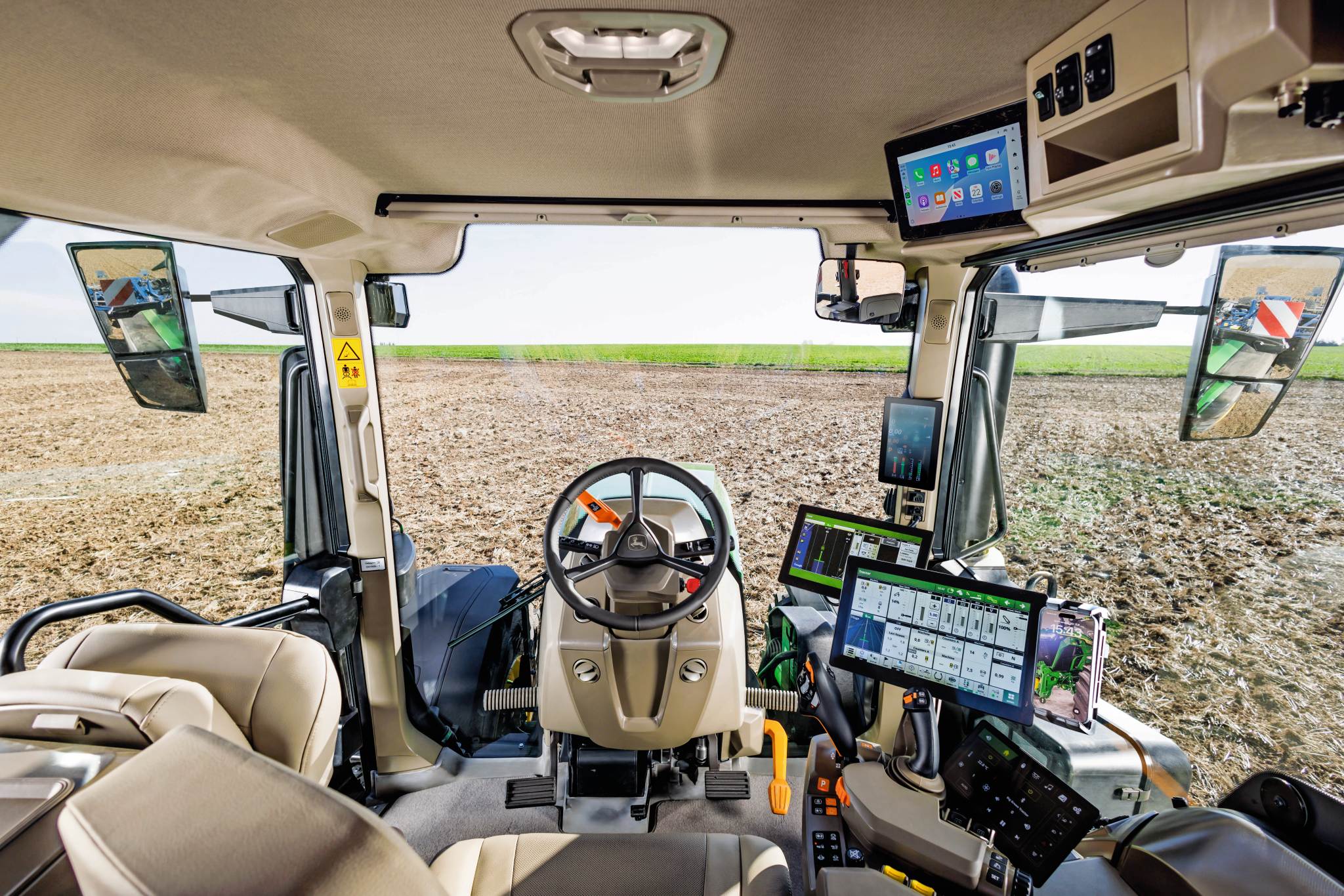 Modern cabine-interieur van de tractor met stuurwiel, touchscreen-displays en bedieningselementen voor precisielandbouw met uitzicht op een gecultiveerd veld