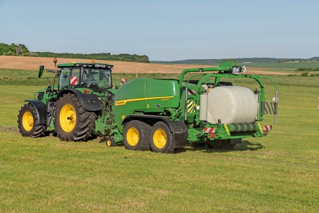Presse enrubanneuse John Deere C442R tirée par un tracteur John Deere 6R 185 formant des balles d’ensilage à haute densité