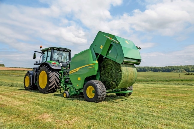 Presse à balles John Deere F442M tirée par un tracteur John Deere 6M éjectant une balle d’herbe