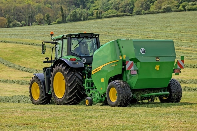 Presse à balles John Deere F442M tirée par un tracteur John Deere 6M dans un champ d’herbe vallonné