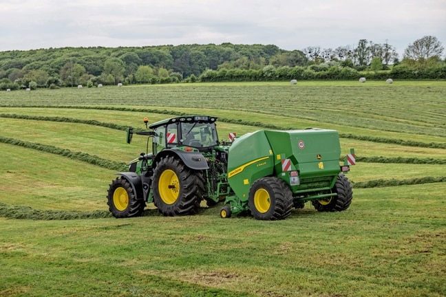 Presse à balles John Deere F442R tirée par un tracteur John Deere 6M dans un champ d’herbe vallonné