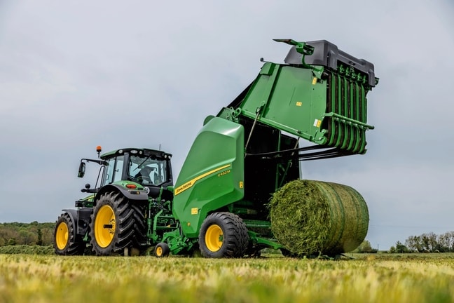 Presse à balles John Deere V462M tirée par un tracteur John Deere 6M éjectant une balle d’herbe
