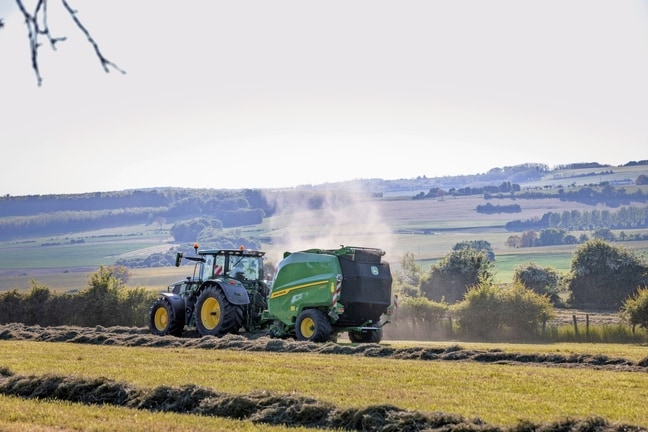 John Deere V462R tirée par un tracteur John Deere 6R 185 pressant du foin