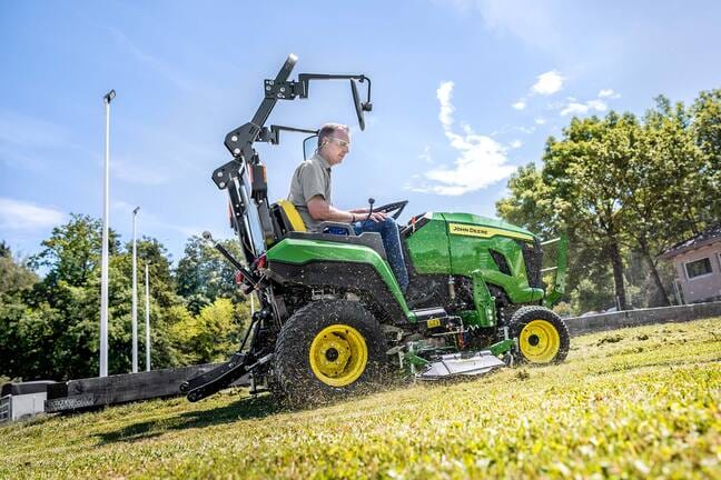 Un utilisateur tondant une pente herbeuse à l’aide d’un tracteur compact John Deere équipé d’une unité de coupe ventrale