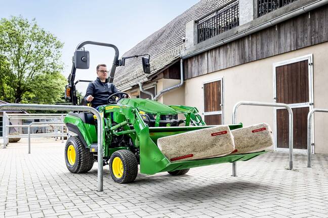 Tracteur compact John Deere transportant deux balles de litière pour animaux dans le godet de son chargeur frontal